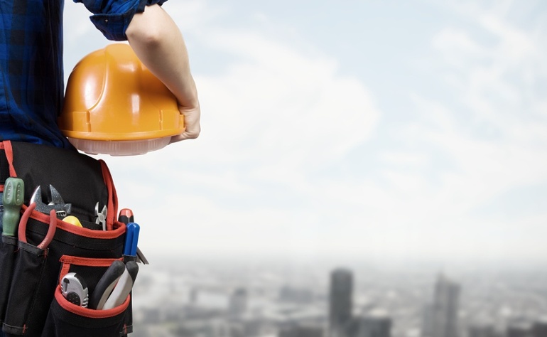 Close up of woman mechanic with yellow helmet in hand against city background.jpeg