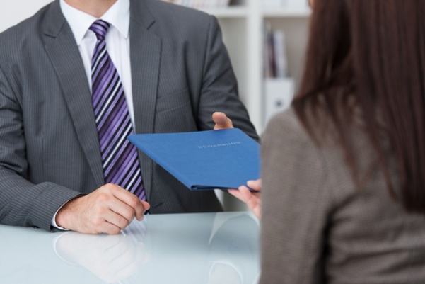 Employment interview with a close up view of a female applicant handing over a file containing her curriculum vitae to the businessman conducting the interview.jpeg